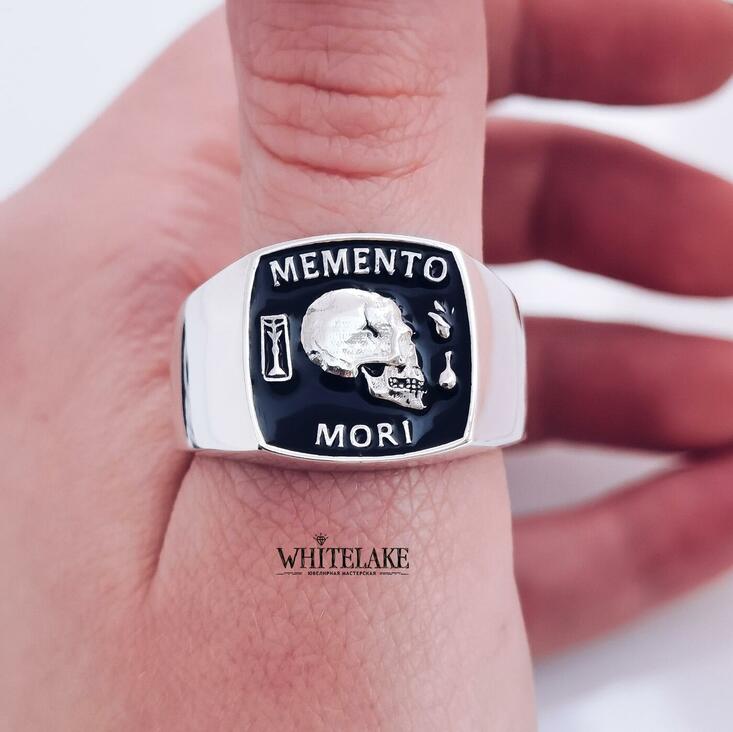 Красивое кольцо-печатка из золота с белой надписью Memento Mori, надетое на большой палец левой руки