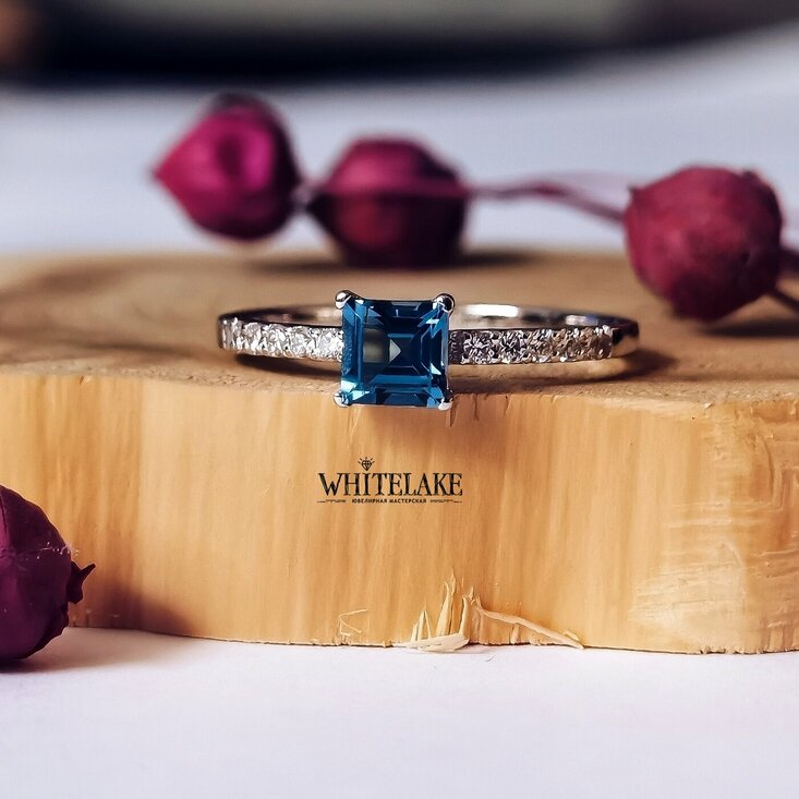 Кастомное помолвочное кольцо из белое золота с топазом London blue на дереянной подставке