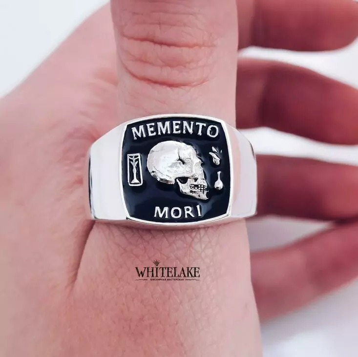 Красивое кольцо-печатка из золота с белой надписью Memento Mori, надетое на большой палец левой руки
