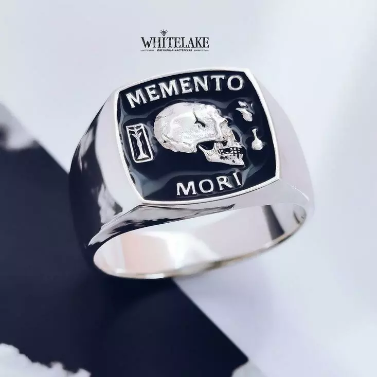 Кастомная мужская печатка с черепом и надписью Memento Mori, сделанная из белого золота и лежащая на столе
